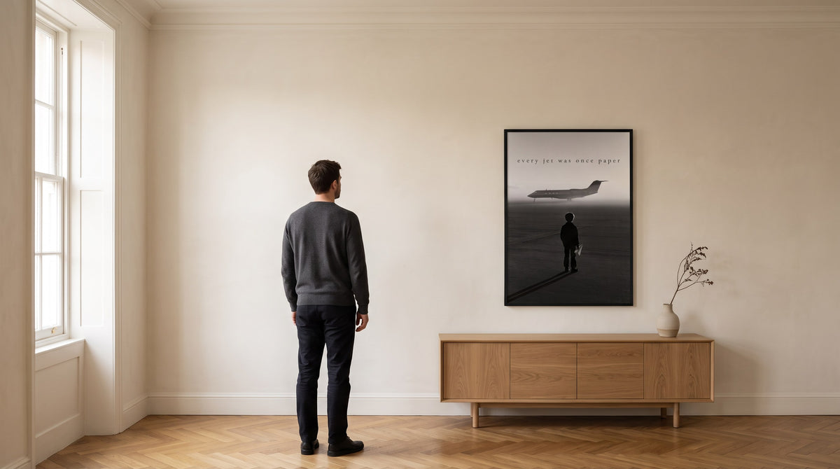 A man seen from behind looking at the framed print IL PRIMO VOLO on a plaster wall in a London apartment